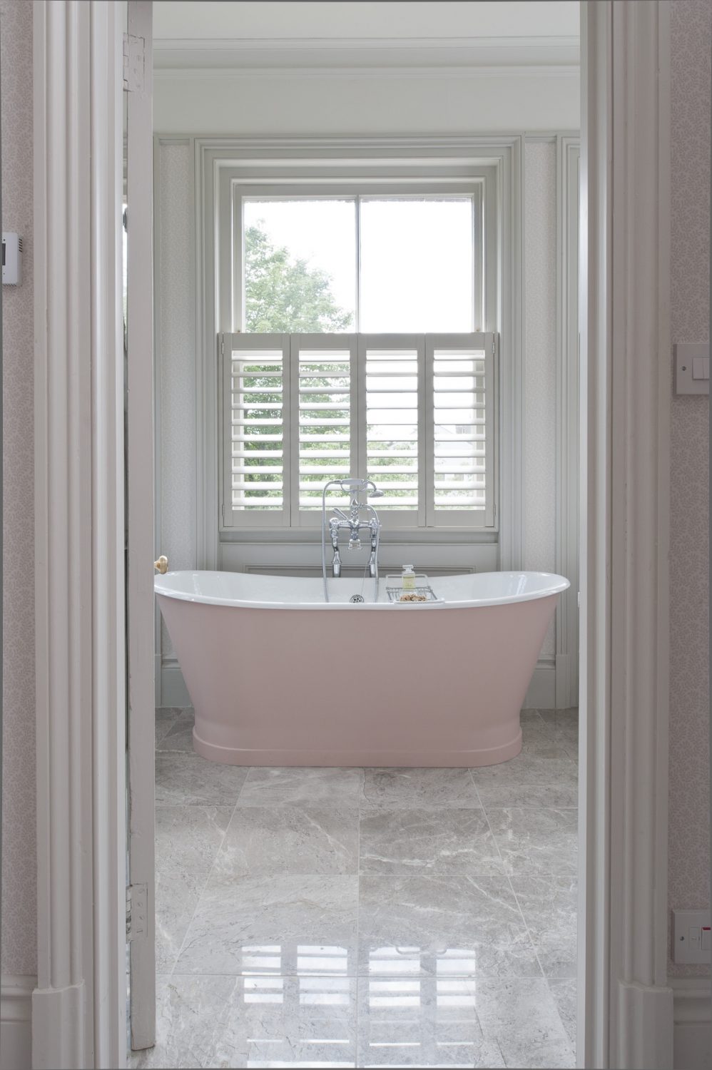 The shell pink bath sits in the centre of the marble-floored master bathroom; shutters provide privacy without losing light