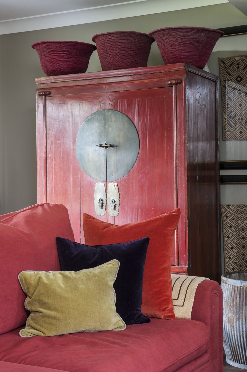 To the left of the woodburner, echoing the vibrant red of the sofa in front, stands a striking Chinese wedding cabinet