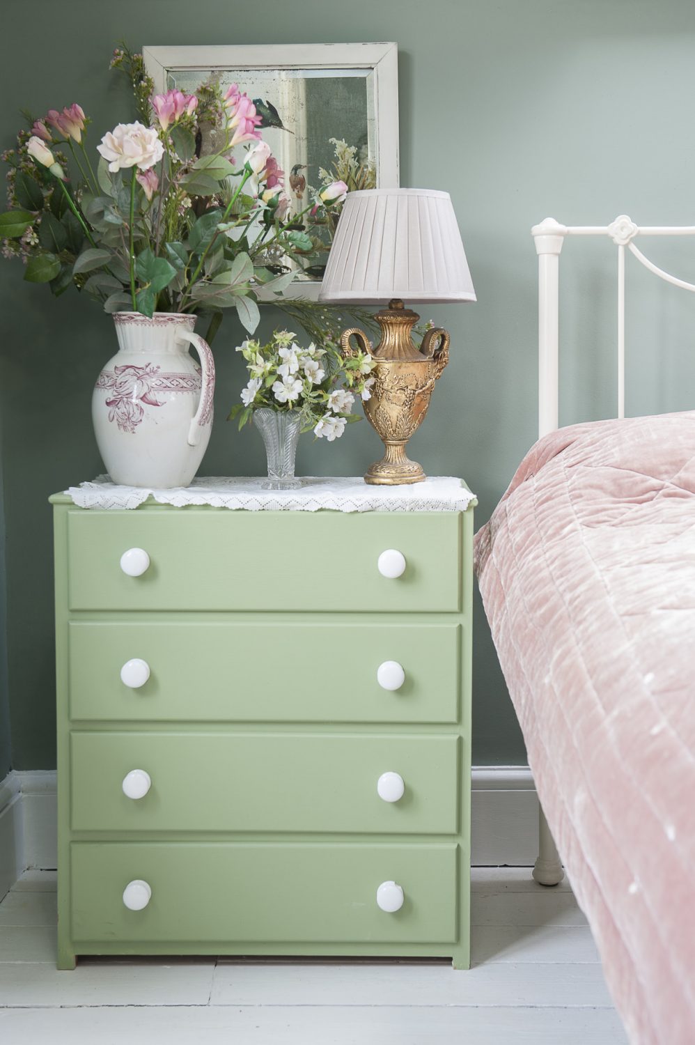 Vases of flowers in soft pastel shades complement the classic white Laura Ashley bed frame and freshly painted green chest of drawers