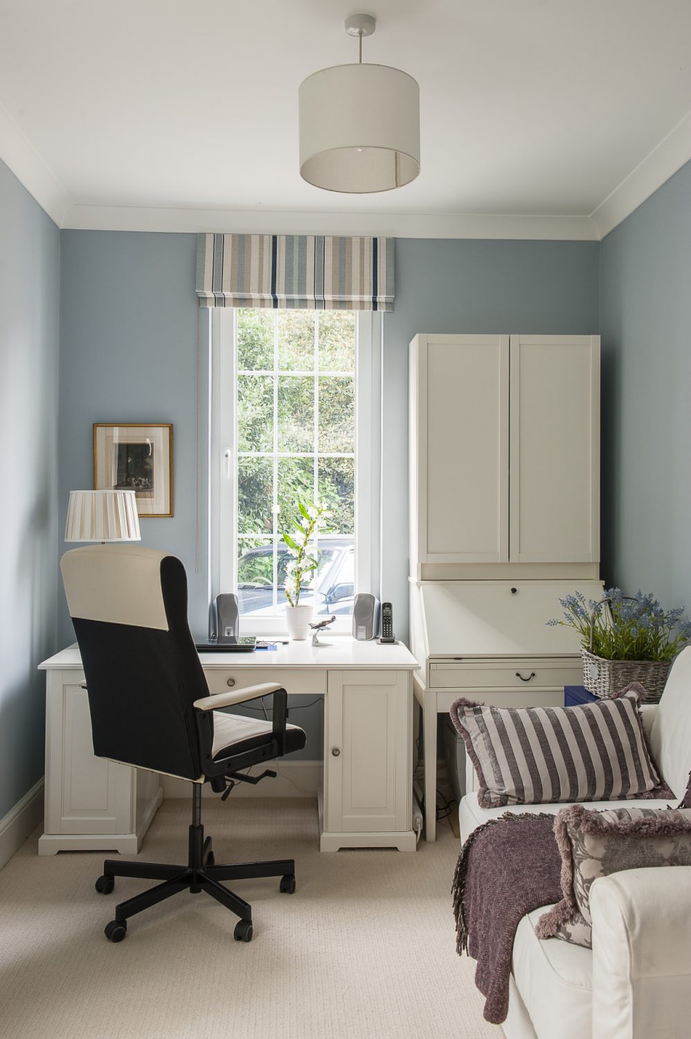 The study is painted in a cool blue and furnished simply with white painted bureau and desk