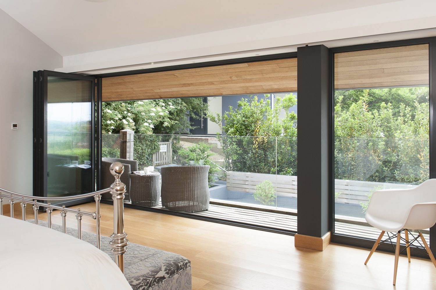The wall of bi-folding doors is echoed upstairs in the master bedroom directly above the kitchen where they open out onto a decked balcony and more Lloyd Loom surrounded by a plate glass balustrade