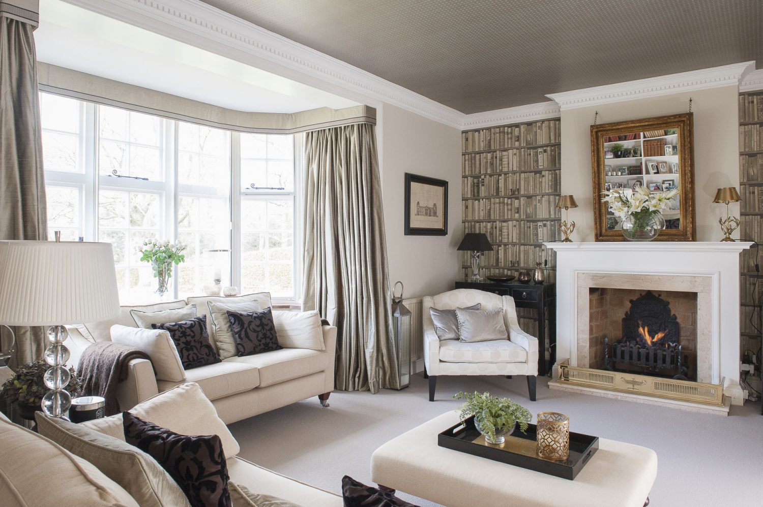 On either side of the fireplace, the alcoves are papered with Andrew Martin’s faux books and over the mantelpiece, Victoria has hung a gilt mirror from a heavy antique chain that, cleverly, tilts the looking glass in a downward direction, reflecting the room