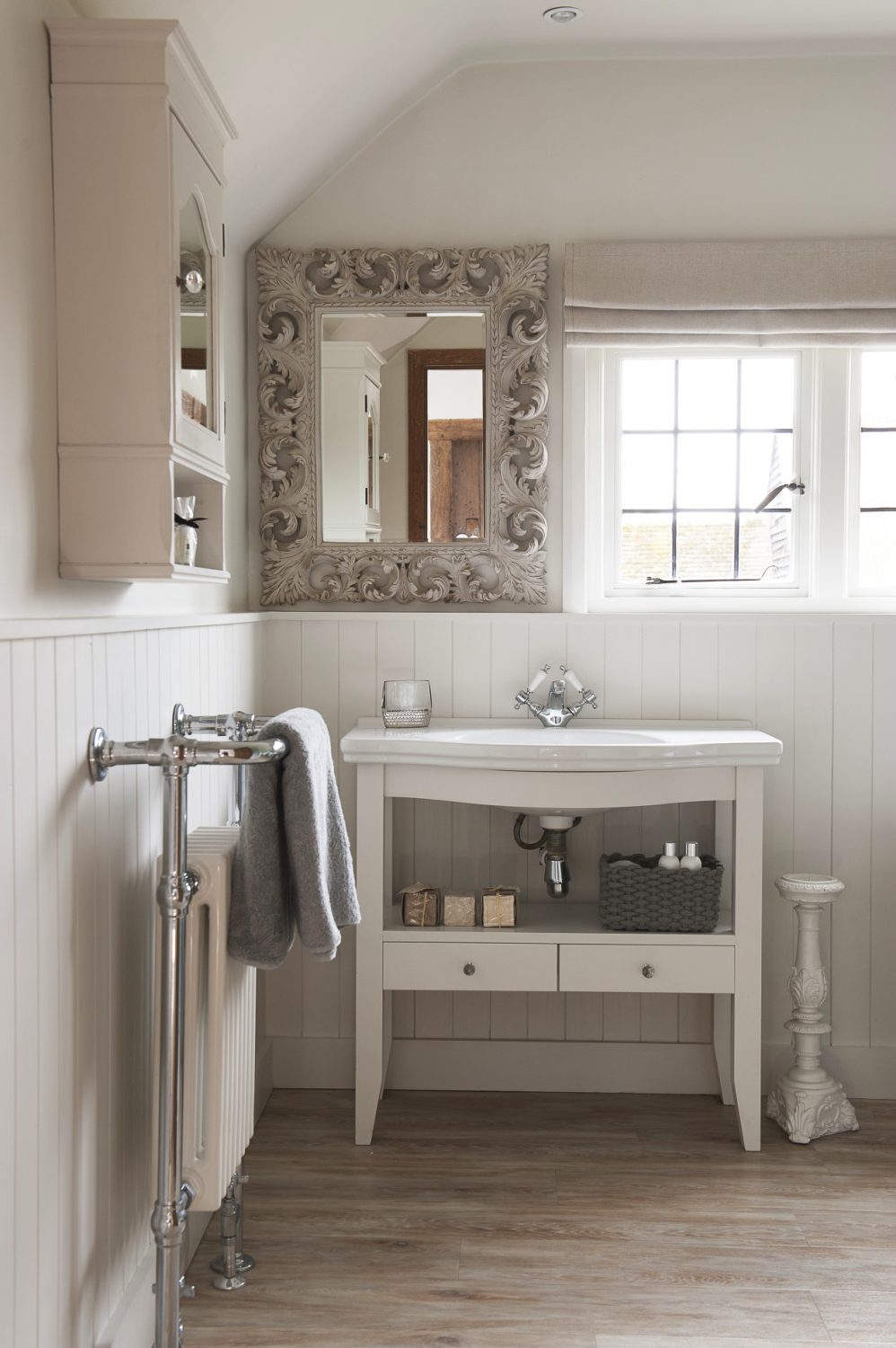 An ornate mirror is a feature in the classic, welcoming bathroom, where tongue-and-groove panelling adds a country cottage feel alongside the painted wood sink unit