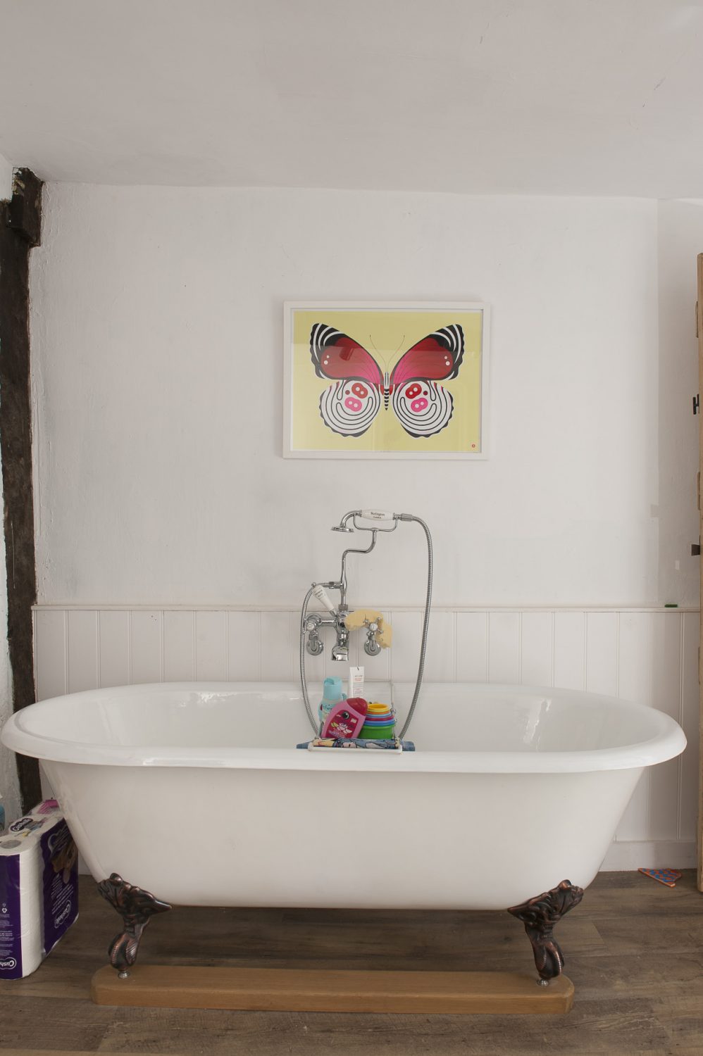 the butterfly print above the bath adds a playful and colourful touch to the otherwise pale interior