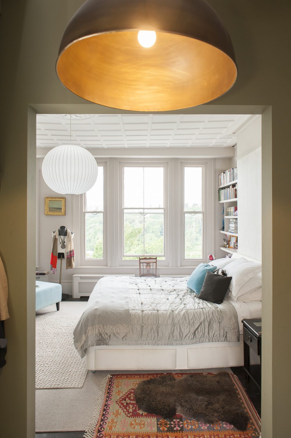 The pale grey bedroom is linked to the bathroom by an olive green dressing room. The striking copper light fitting is by Jim Lawrence. The seascape on the far wall is by Anne Packard. The white and steel pendant light is one of a number of George Nelson classic lights throughout the house