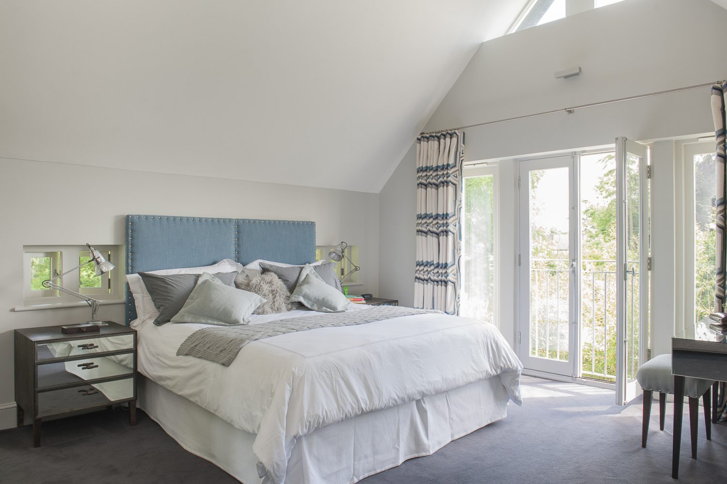 The master bedroom is flooded with light from a vaulted ceiling and French windows onto a Juliet balcony, further enhanced by Jane’s choice of pale grey for the walls, bed linen and the background colour in the Larsen graphic weave fabric of the curtains. The windows on either side of the bed act like extensions of the upholstered headboard, with a pleasing symmetrical effect. The mirrored side tables, specially designed by Nathan for this room, further bounce the light around, as do the chrome bedside lamps which are original vintage Anglepoise