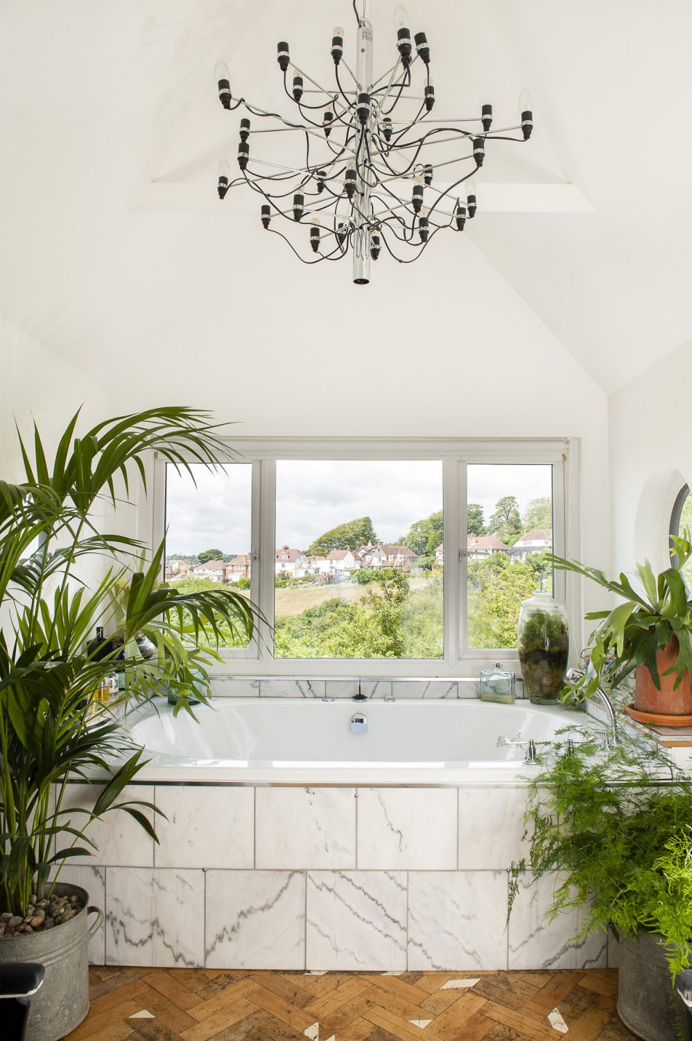 The plant-filled master bathroom has views over the Bourne valley. The chandelier is a 1958 design by Gino Sarfatti from Flos