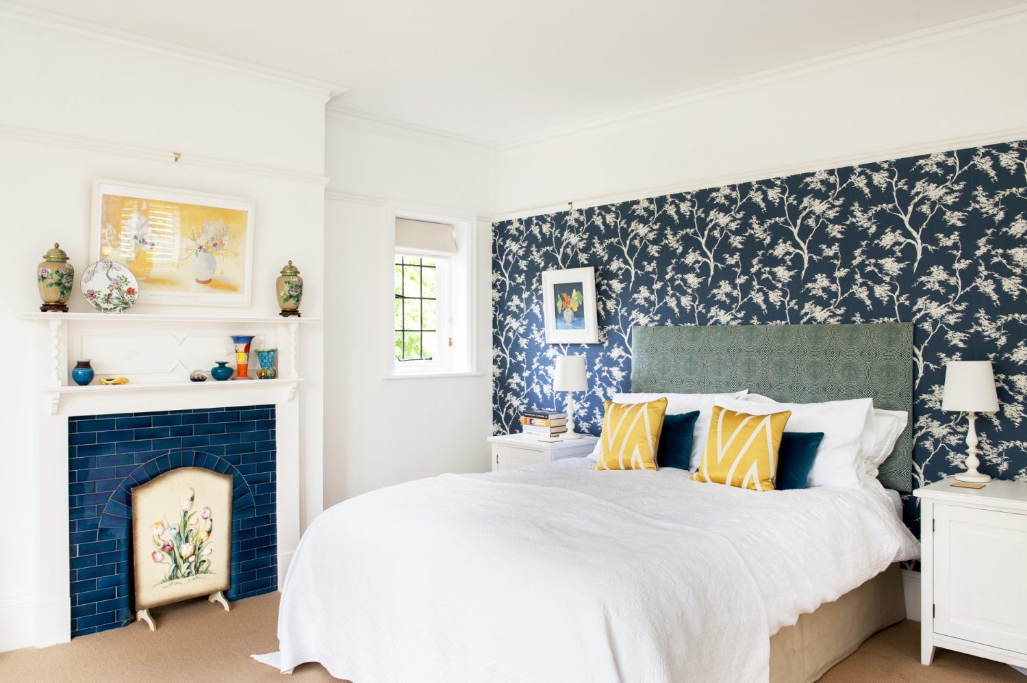 With off white walls on three sides and a lovely shade of indigo patterned wallpaper on the fourth – which picks up the blue tiles of the fireplace – it is a very calm room