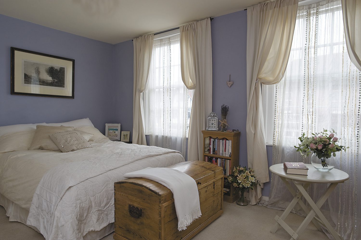 the main bedroom has lilac walls and ivory curtains. The lithograph above the bed is French