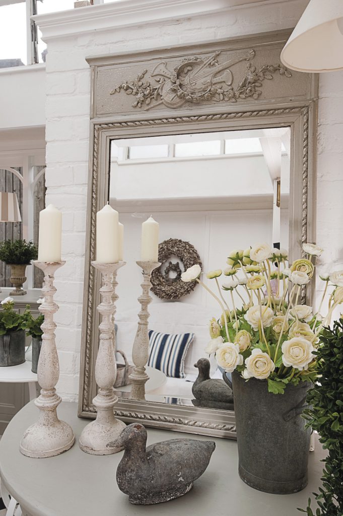 a pretty mirror and a pair of candlesticks, as well as more faux flowers in the form of ranunculus and tall white delphiniums, enhance the conservatory