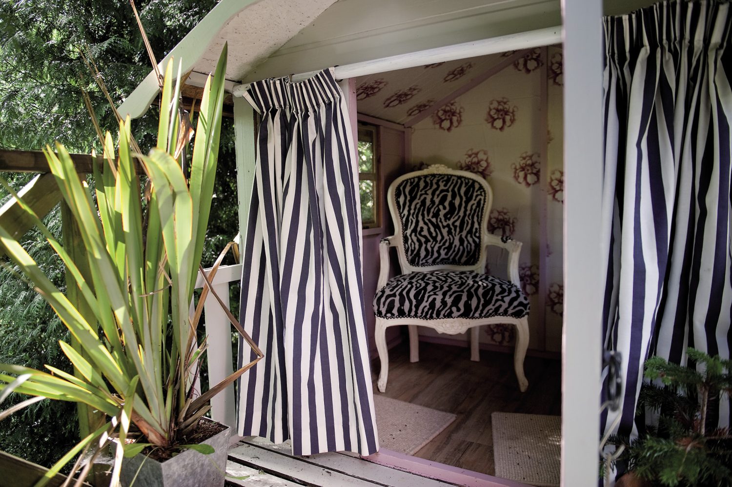 Down another set of steps and there, among the boughs of a fine oak tree is the treehouse, now painted white, with nautical blue and white striped curtains. Inside, Andrew has wallpapered it and added just one, throne-like chair