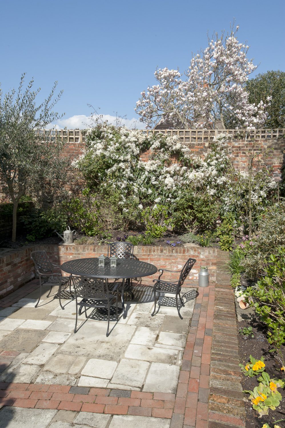 The peaceful, sheltered courtyard features high walls covered in climbing roses and fragrant clematis armandii. Raised brick beds are planted with hydrangeas, camellias, lavender and pinks