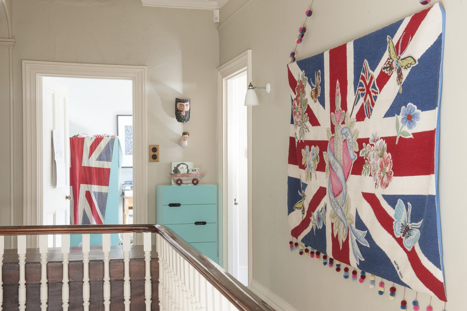 A giant embroidered and beaded Union Jack tapestry hangs boldly on one wall, whilst a comfy armchair is placed next to a set of full-to-bursting bookshelves