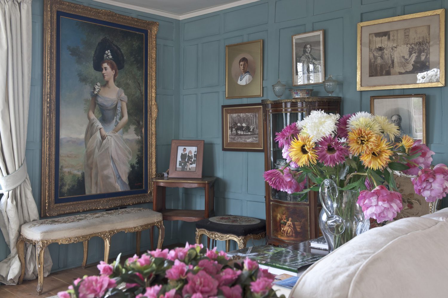 The panelled walls of the drawing room have been painted ballroom blue which perfectly offsets the gilt framed portraits around the room