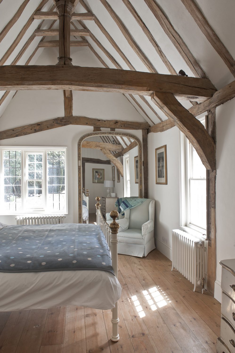 The room beyond is the bedroom where the warm, honey coloured timbers are offset by fresh blue and white linens on the bed and armchair