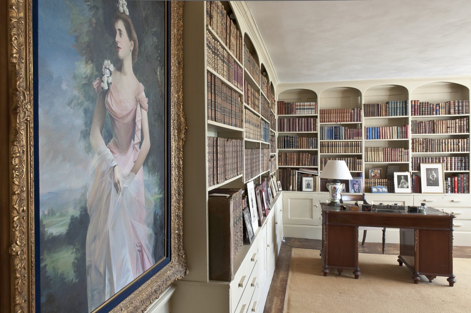 The library walls are painted a soft ochre yellow and two sides of the room feature floor to ceiling cupboards and shelves that support hundreds of leather-bound books.