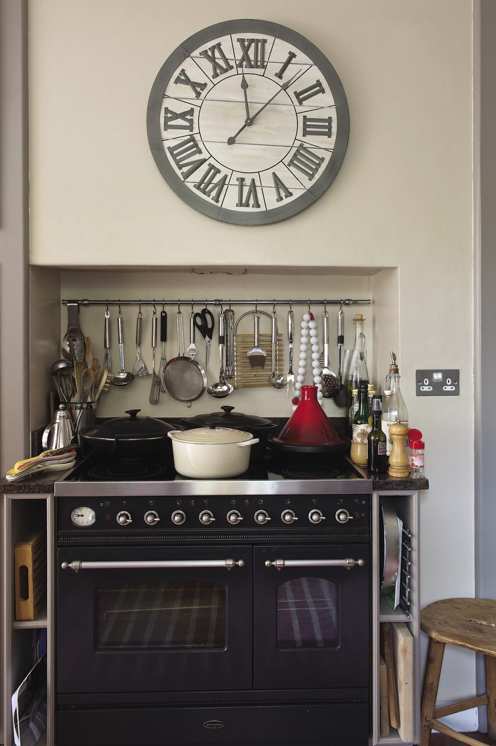 A large wooden clock with bold Roman numerals that was bought from Maison in Tunbridge Wells hangs above the wide black cooking range