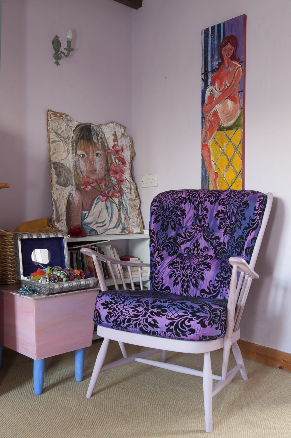 In one corner of Oeda’s bedroom, a wooden armchair is upholstered in striking mauve and black. On the walls are more pictures by her daughters and a nude by Kim Langford