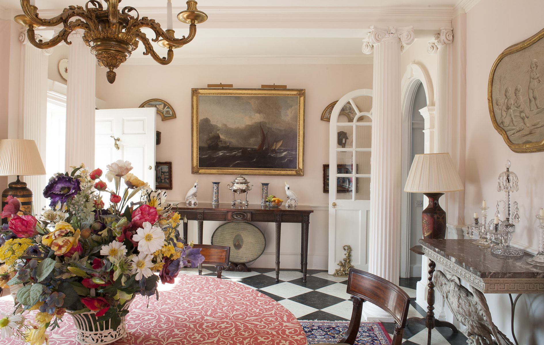 The large reception hall and dining room features a handsome marble fire surround, a marble bust on a tall plinth and a pair of marble-topped tables and walls painted in Pink Ground by Farrow & Ball