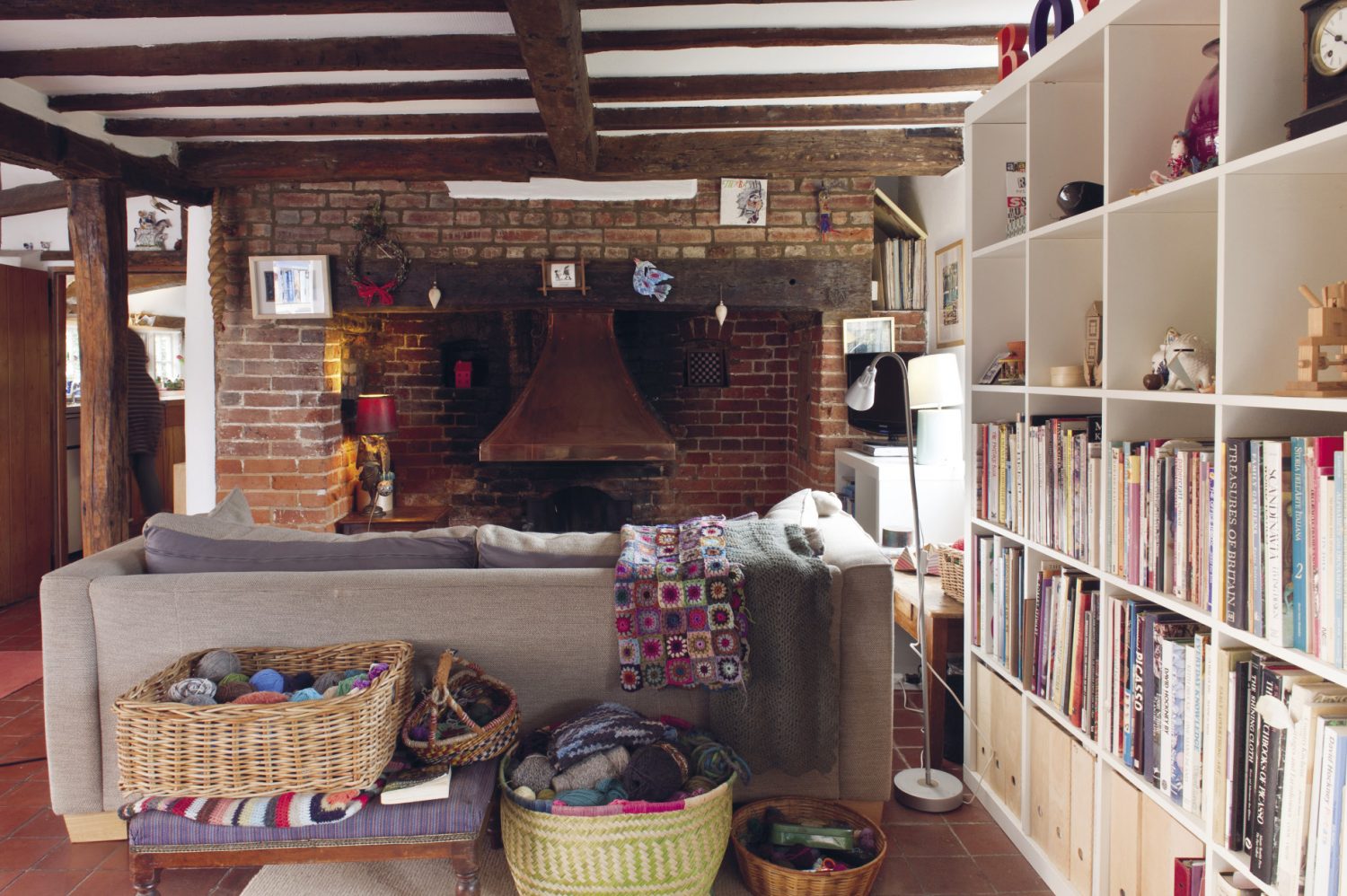 In the sitting room, a large ecru linen-covered sofa faces an inglenook fireplace with baskets of wool stacked all around and behind it