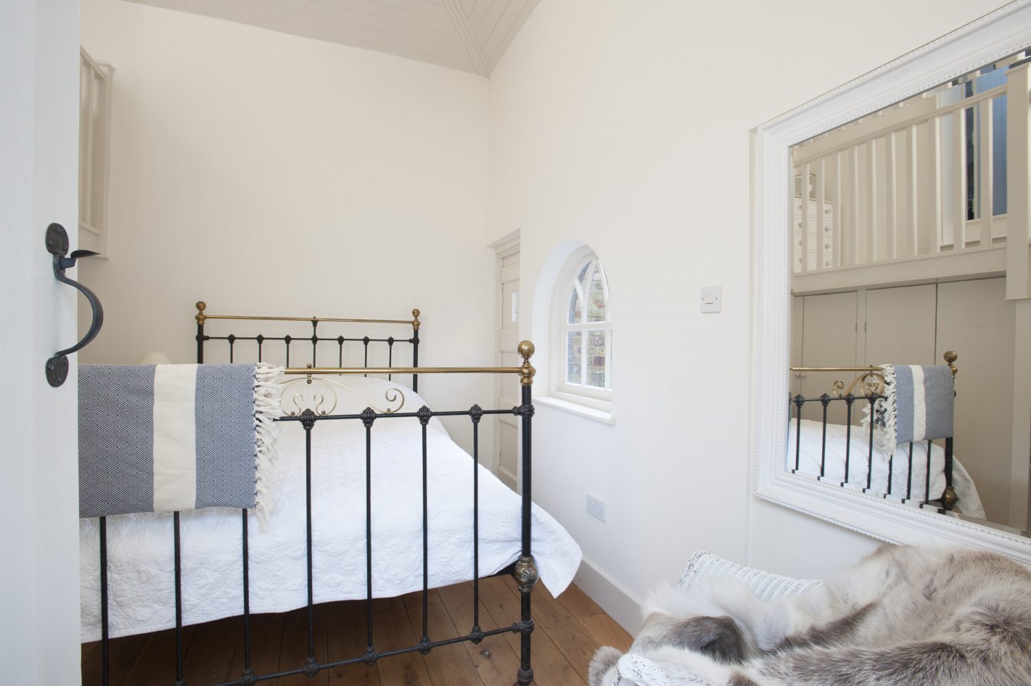 The original shed has been converted into a cosy white-on-white guest bedroom with a brass and iron bedstead