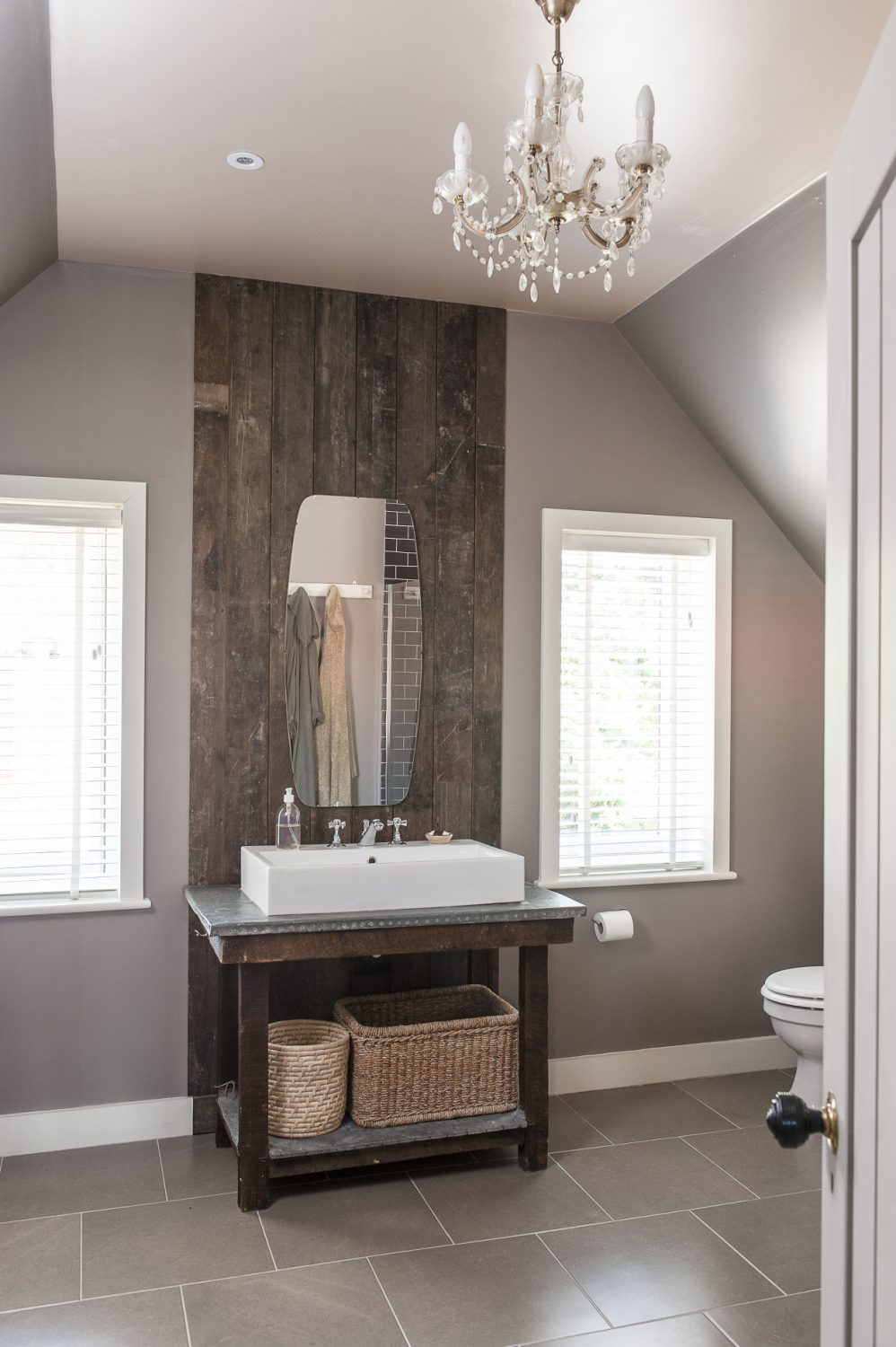 The bathroom is a gentle mushroom with cool white woodwork. The basin sits on an antique lead-topped table backed by a ceiling height panel made from reclaimed floorboards