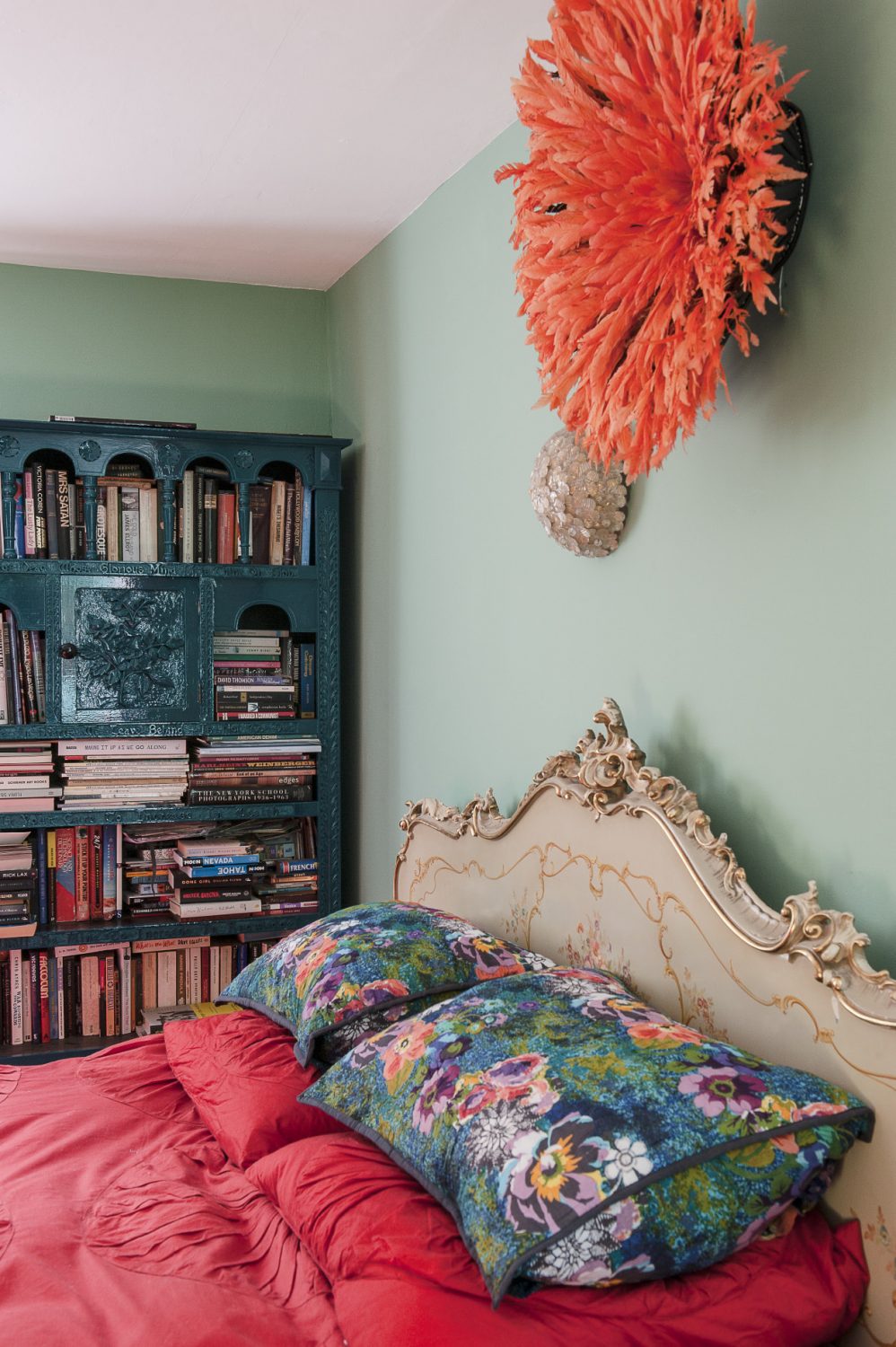 The bedroom features a 1950s Italian gilded bed above which is mounted an orange feathered headdress from the Cameroon
