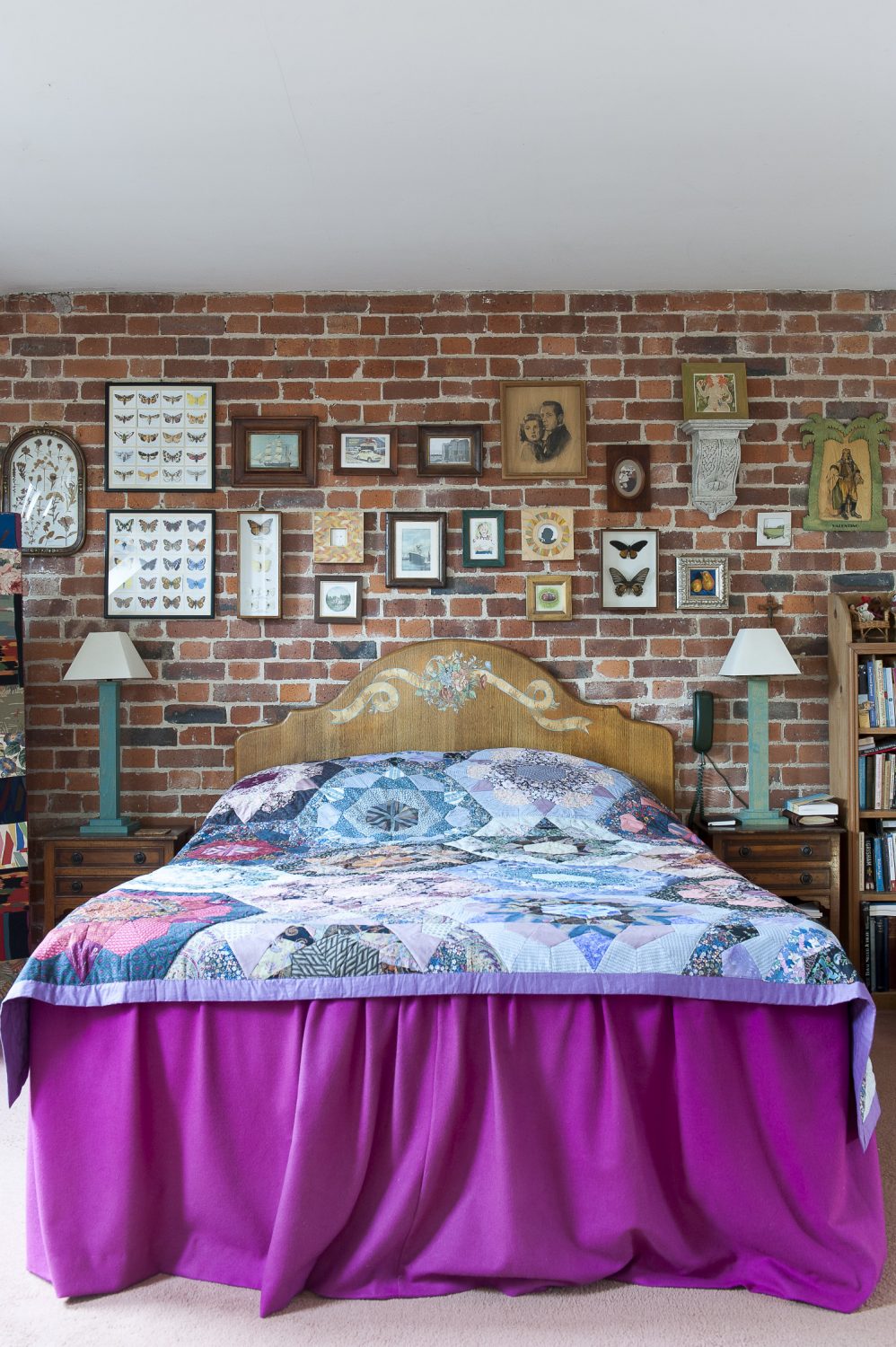 Collections of framed butterflies and portraits line the bare brick wall in the master bedroom. The quilt was handmade locally