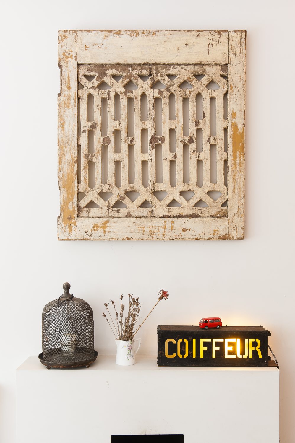 An old French chateau shutter on the living room wall is displayed like a piece of art above an illuminated coiffeur unit from a French hairdresser’s, picked up in Lille at the Braderie France, a massive flea market
