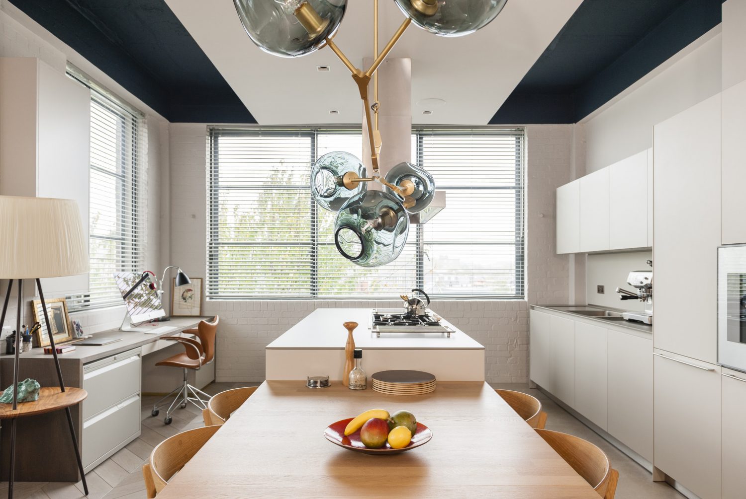 The kitchen, with its sculptural chandelier by Lyndsey Adelman, blends seamlessly into the living room. Adjacent to the kitchen, a desk unit acts as a home office