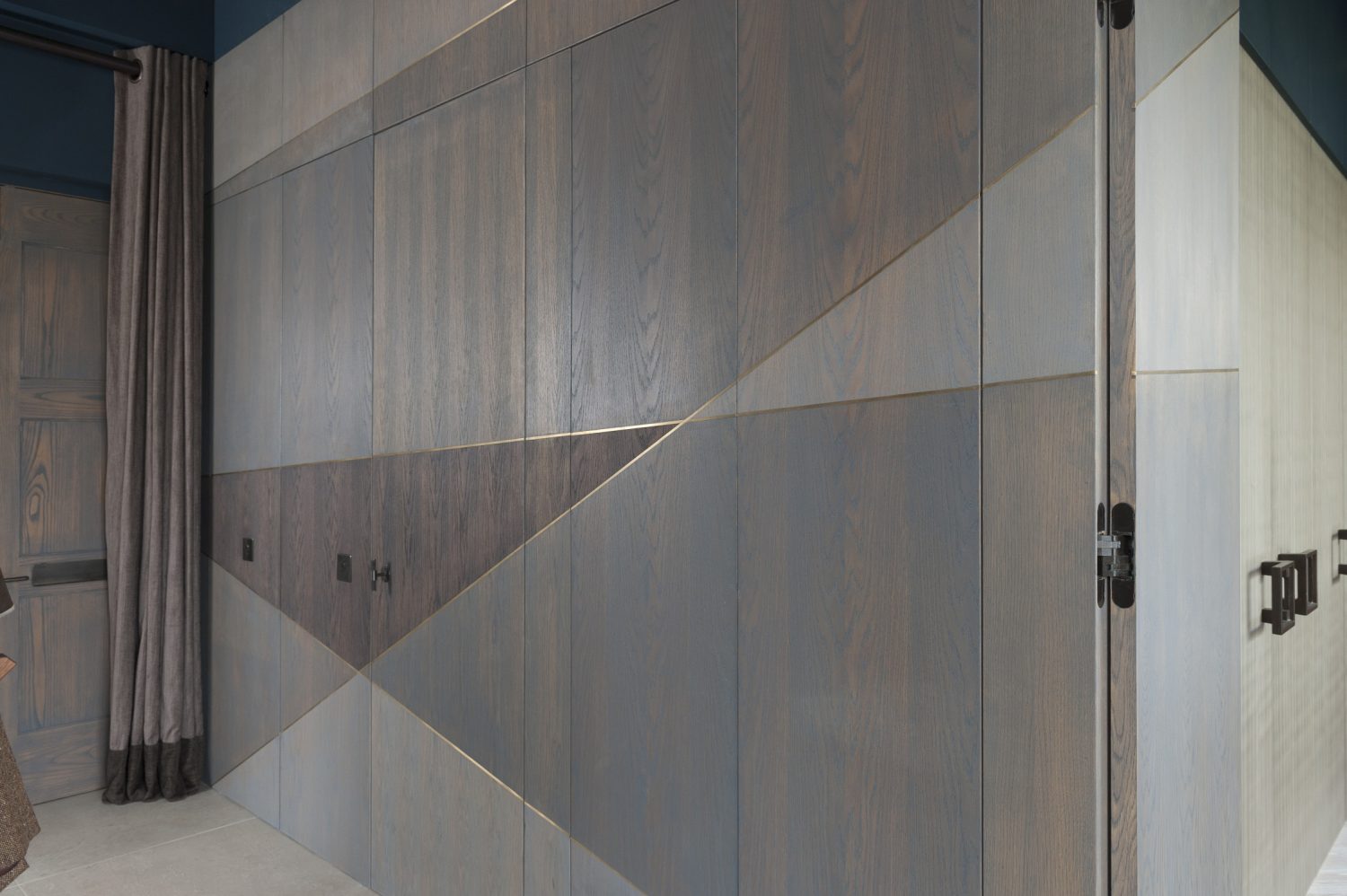 The linear brass inlays are picked up as a theme on the walls too, which are also made from grey stained oak. The golden lines serve to unite and streamline the space, running across the ‘hidden’ doors to the bedroom, bathrooms and a storage area