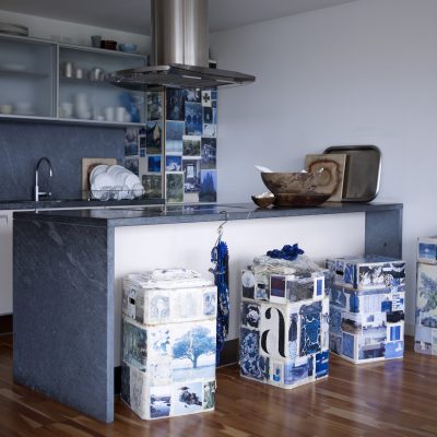 Blue & White: London based creative Ann Shore has put together a striking kitchen with her fresh, arresting palette of white and blue. She has used small pieces of masking tape to cover the fridge in a montage of blue and white images, including old magazine spreads, postcards and printed photos from around the world. Carrying on this theme, Ann has papered her breakfast bar stools – made from tall cardboard storage boxes – in recommissioned pages from books and magazines, to create a patchwork of memory and nostaglia. Her granite worktop on the cooking island carries on the theme, juxtaposed with crisp white cupboards. Wooden bowls and chopping boards bring in a sense of nature, like pieces of driftwood on a seashore, and contrast with the modern, polished-aluminium extractor hood.