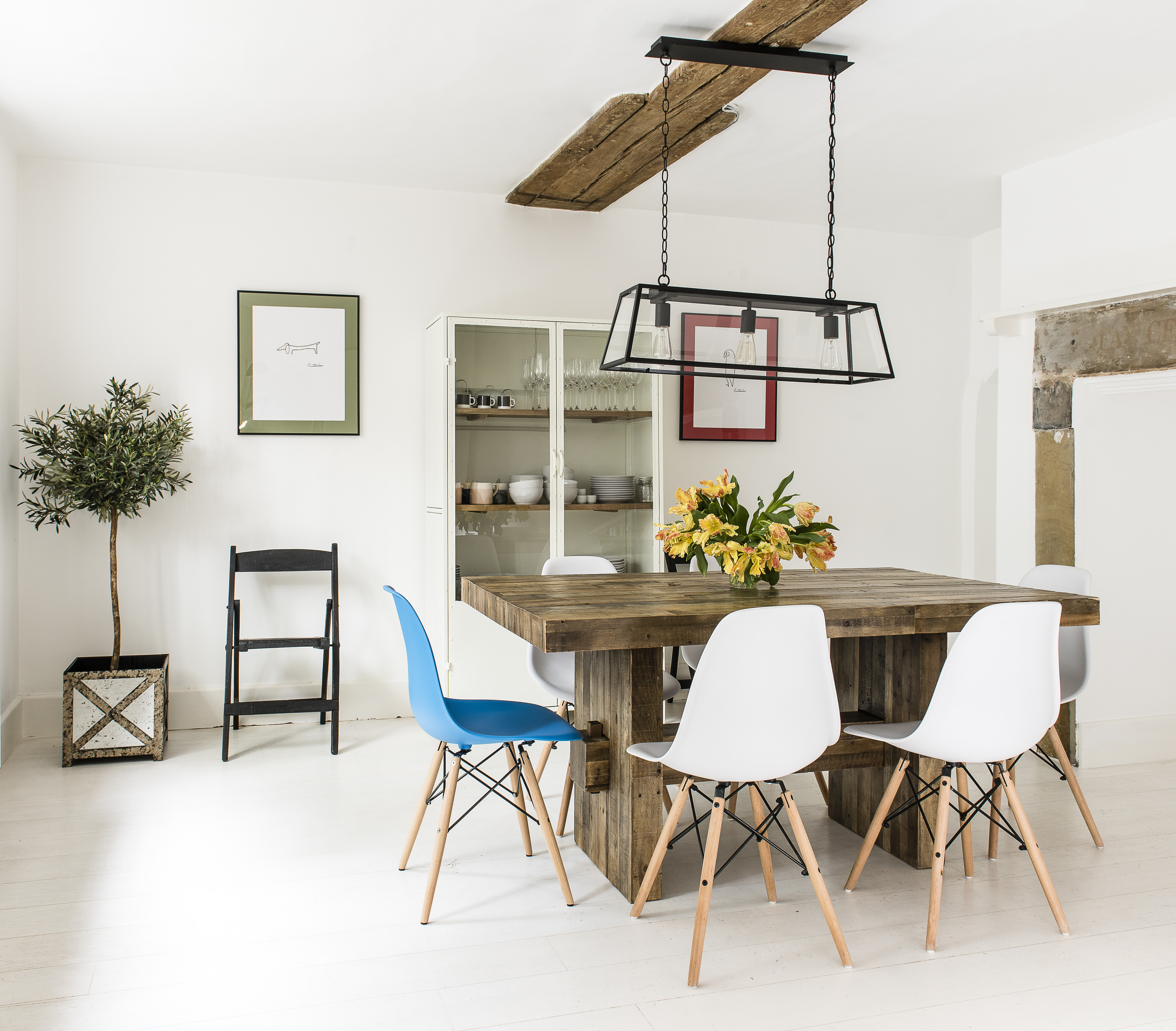 In the family breakfast room, Eames style dining chairs are offset by a chunky oak table, all of which sit below a stripped back central ceiling beam and beside an inglenook fireplace surround.