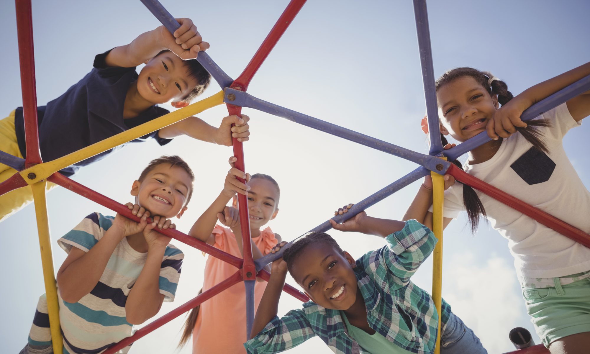 Portrait of happy schoolkids looking through dome climber at school playground