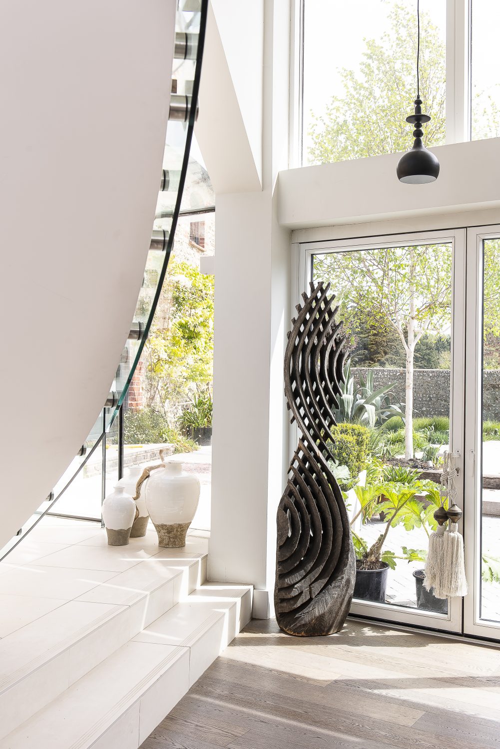 The spacious sitting room forms a link between the two parts of the house. A minimalist modern staircase sweeps up to the first floor and there are glass walls on both sides, looking out to the elegantly planted garden at the front