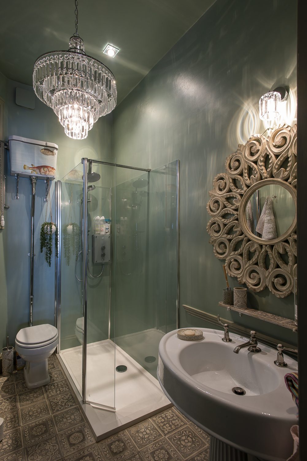A chandelier from nationallighting.co.uk illuminates the sage green shower room, complete with an ornate pedestal basin