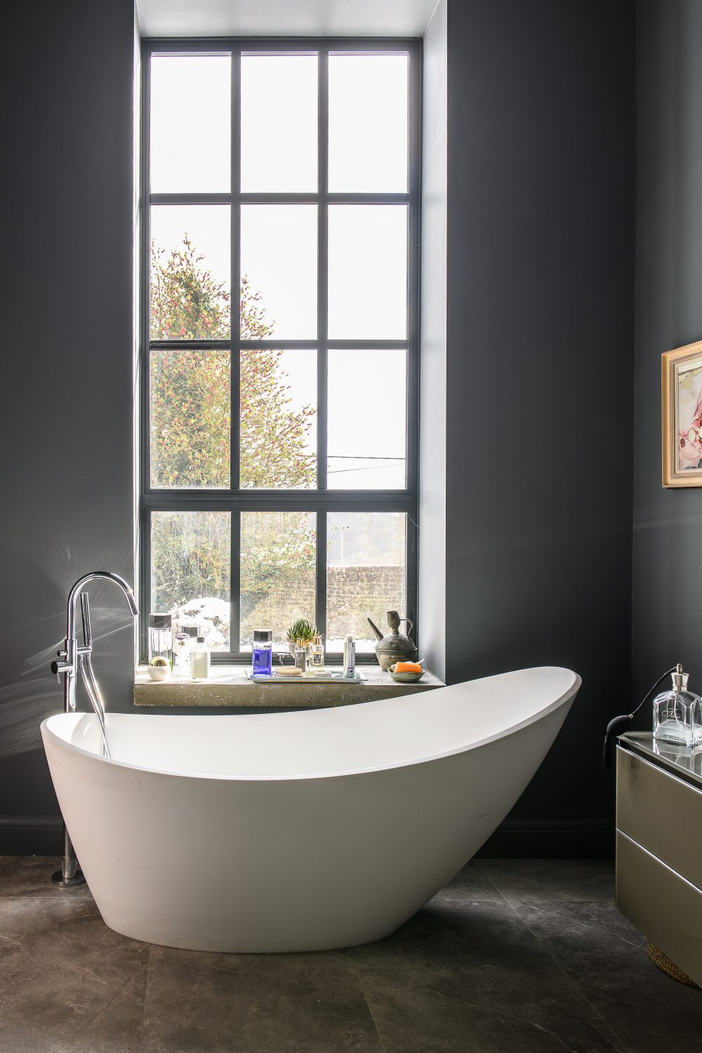 A luxurious, sculptural bath from C P Hart in Tunbridge Wells reclines next to the curtain-less window in the bathroom. The walls are painted in Scree by Little Greene, with wallpaper by Designers Guild
