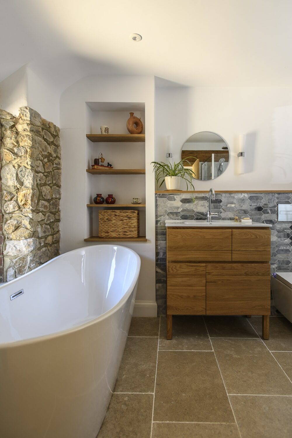 In the family bathroom a freestanding bath curves elegantly against the ragstone wall, while oak shelves and furniture complement the warm, earthy tones of the stone