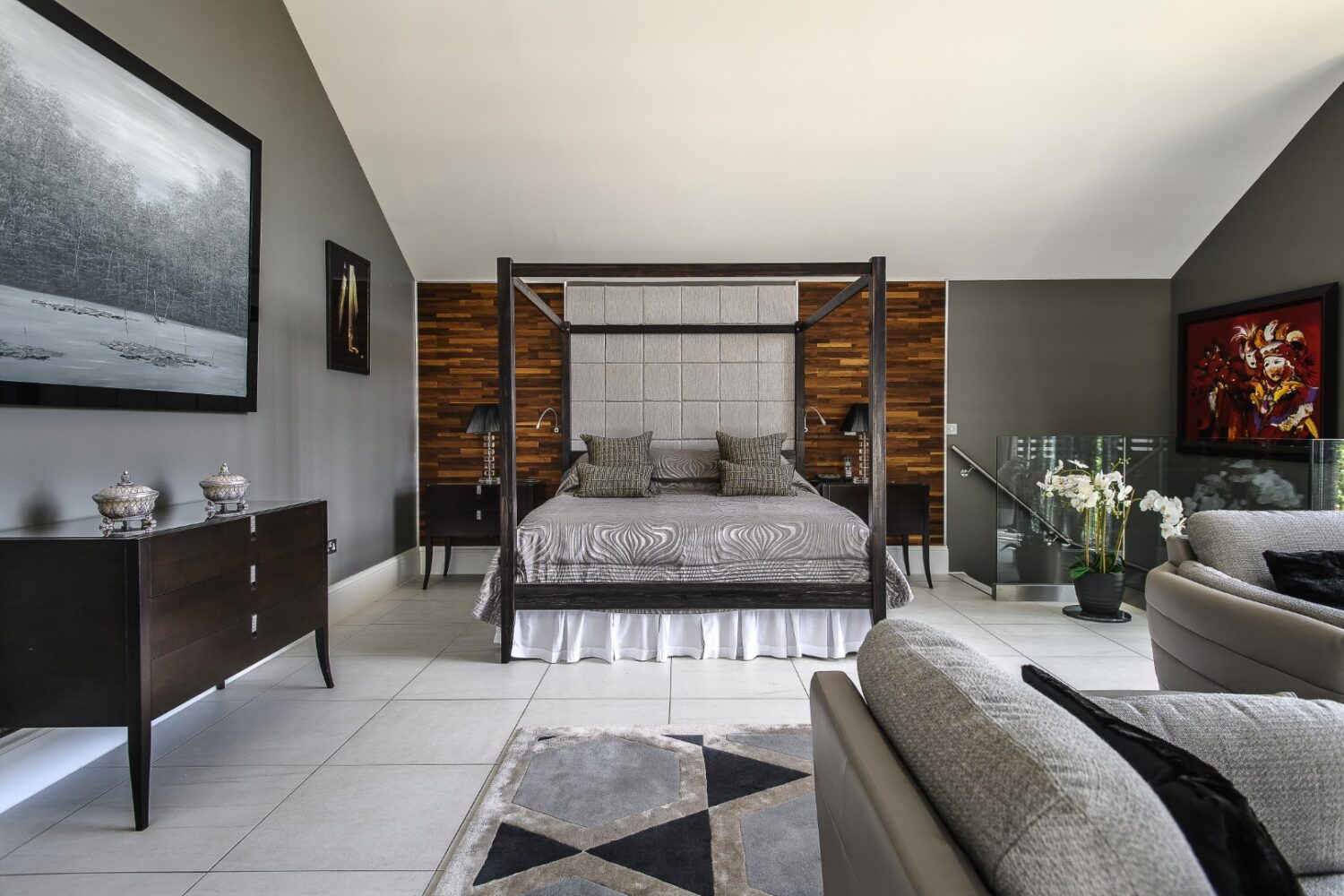 The principal bedroom is dramatic in scale. A four-poster bed stands against upholstered panelling, with a log-burning stove in the corner for winter nights.