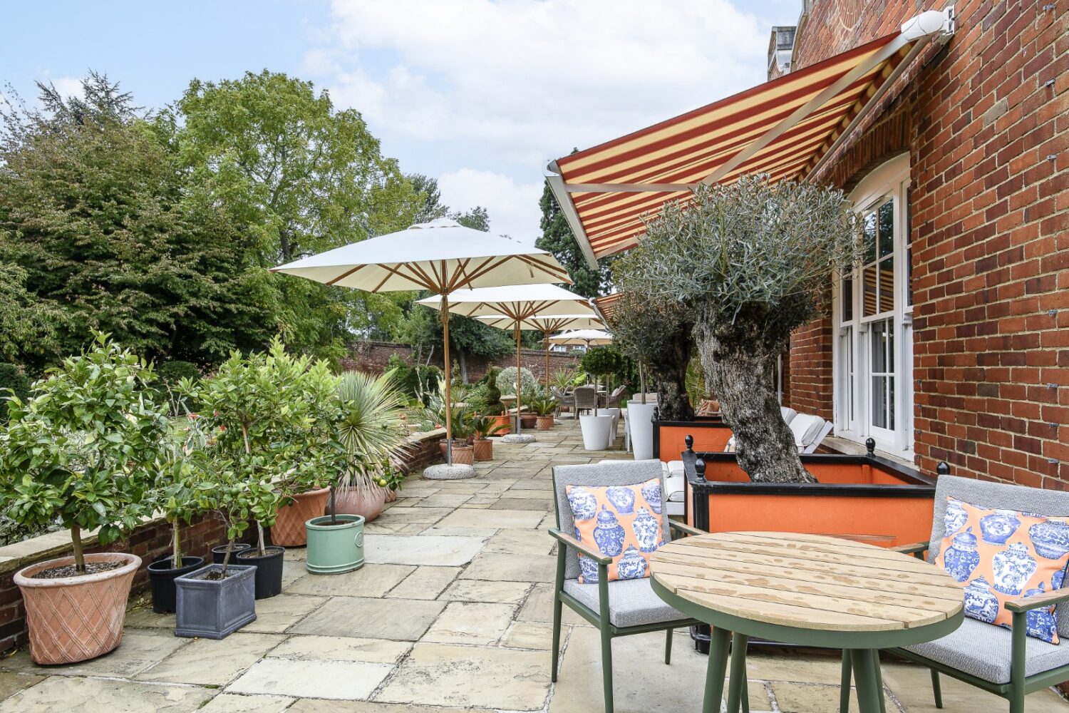 Striped awnings and Mediterranean furnishings lend a holiday feel to the terrace that wraps around the main house