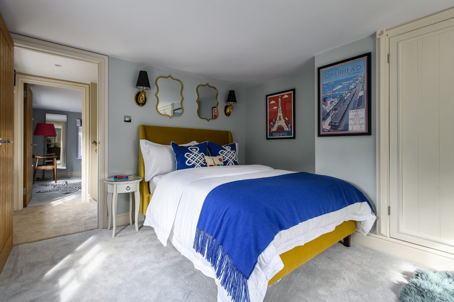 A gold velvet bedstead with electric blue accents alongside bevelled mirrors and gilded wall lights, nods to a sense of Parisian chic