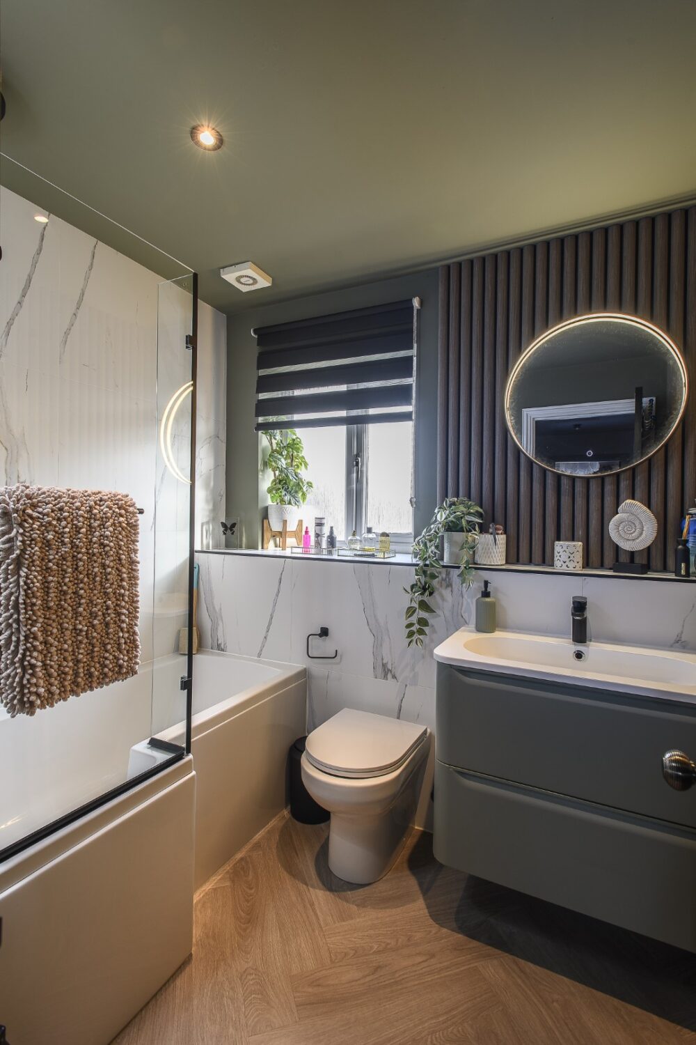 At the end of the landing, the family bathroom is bathed in sage green, while a run of ribbed acoustic paneling adds earthy depth behind the vanity