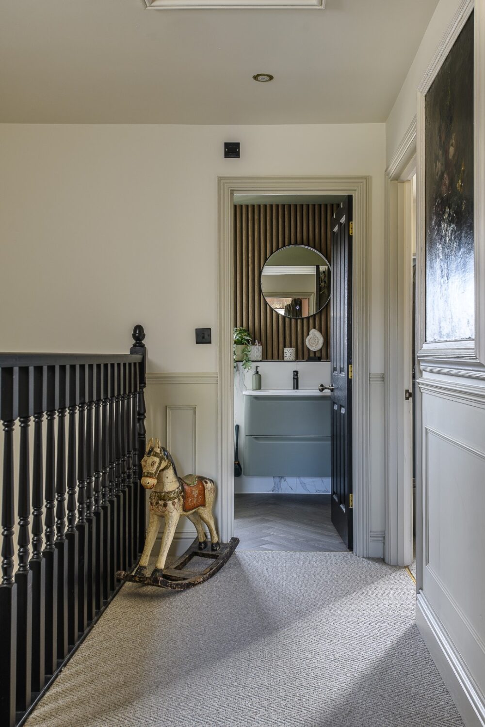 At the end of the landing, the family bathroom is bathed in sage green, while a run of ribbed acoustic paneling adds earthy depth behind the vanity