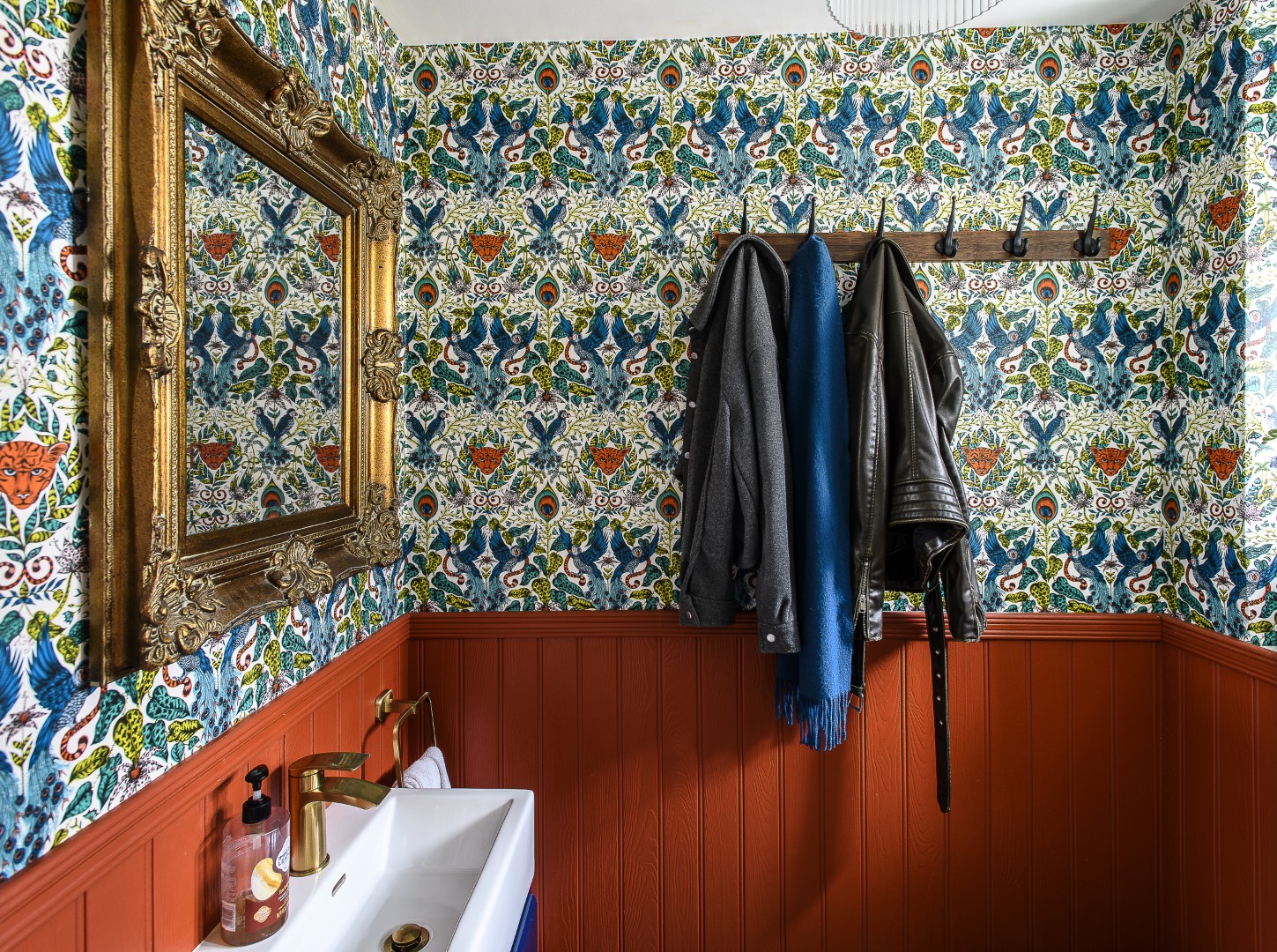 The downstairs cloakroom is wrapped in Emma Shipley wallpaper above spice-orange tongue-and-groove panelling