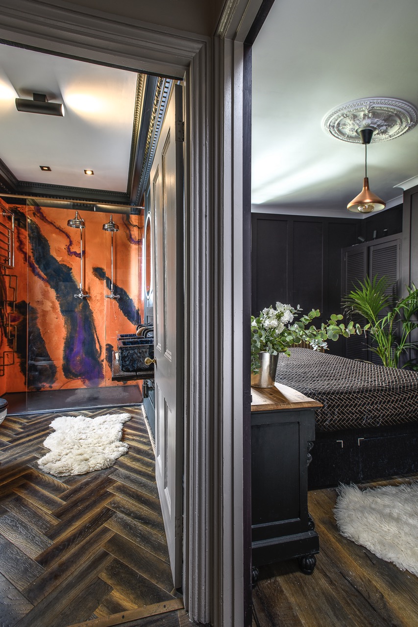 The walk-in shower features a bold experimental epoxy resin finish wall, creating what feels like a molten, abstract backdrop in burnt orange and indigo which pops against the dark tones of the panelled walls.