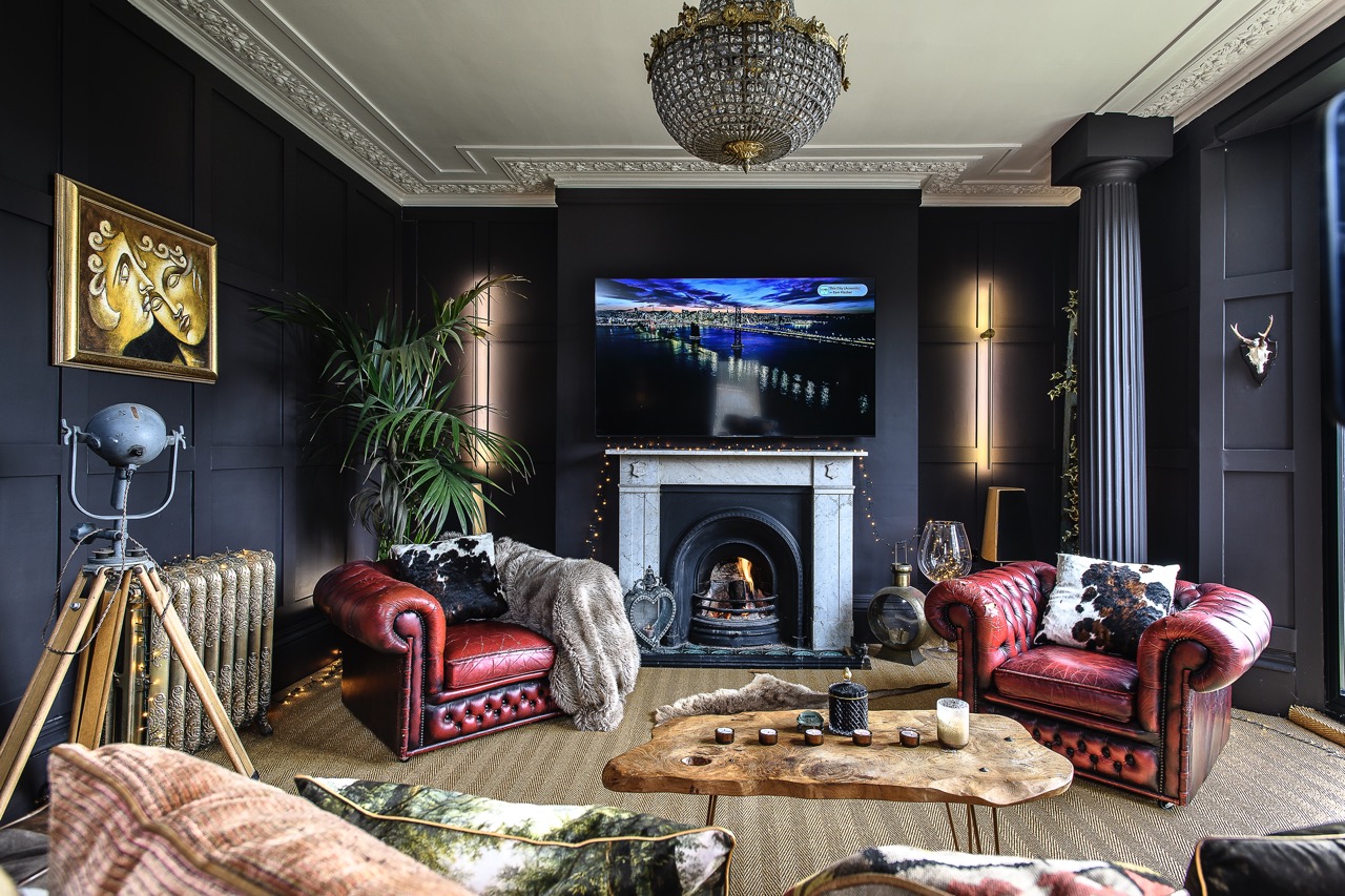 Two red leather Chesterfield armchairs sit against charcoal panelled walls in the sitting room. An original marble fireplace anchors the space.