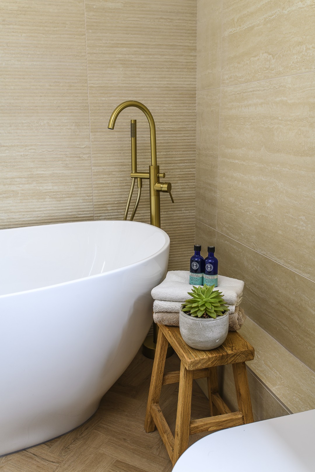 A first floor bathroom is kept contemporary with a curved bath and gold taps which complement the natural tones of the tiles and flooring