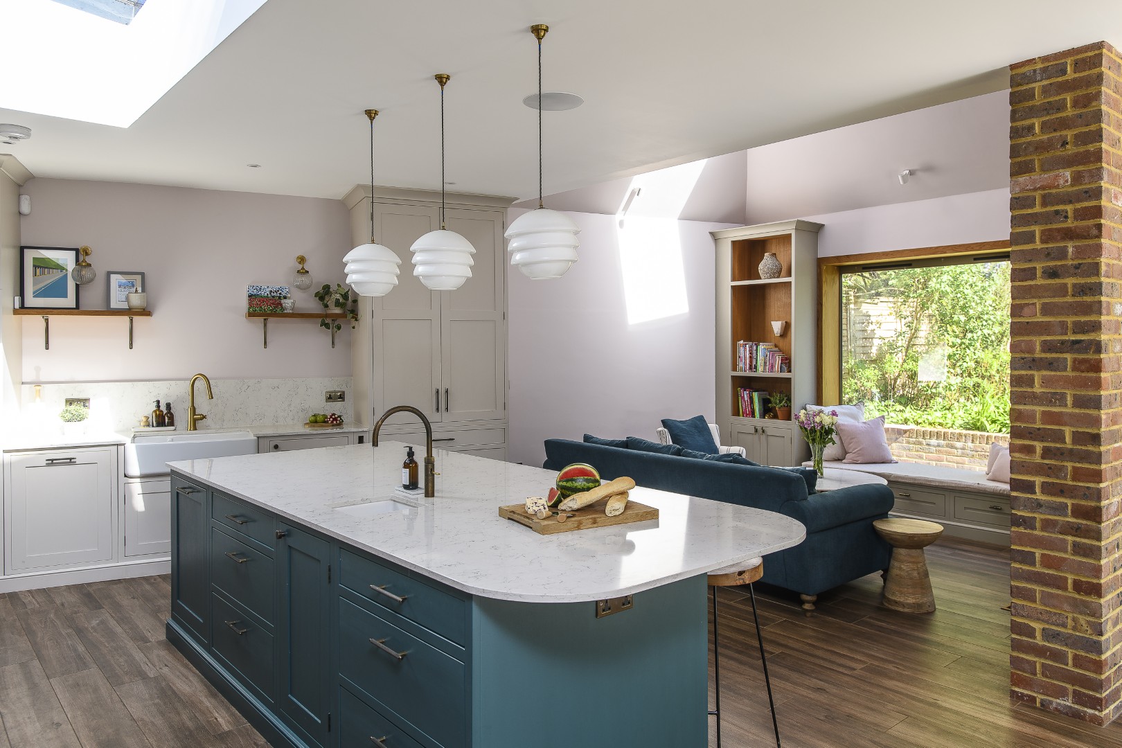 The deep blue-green kitchen island anchors the room, while pale cabinetry and marble surfaces ensure the space remains bright and welcoming.