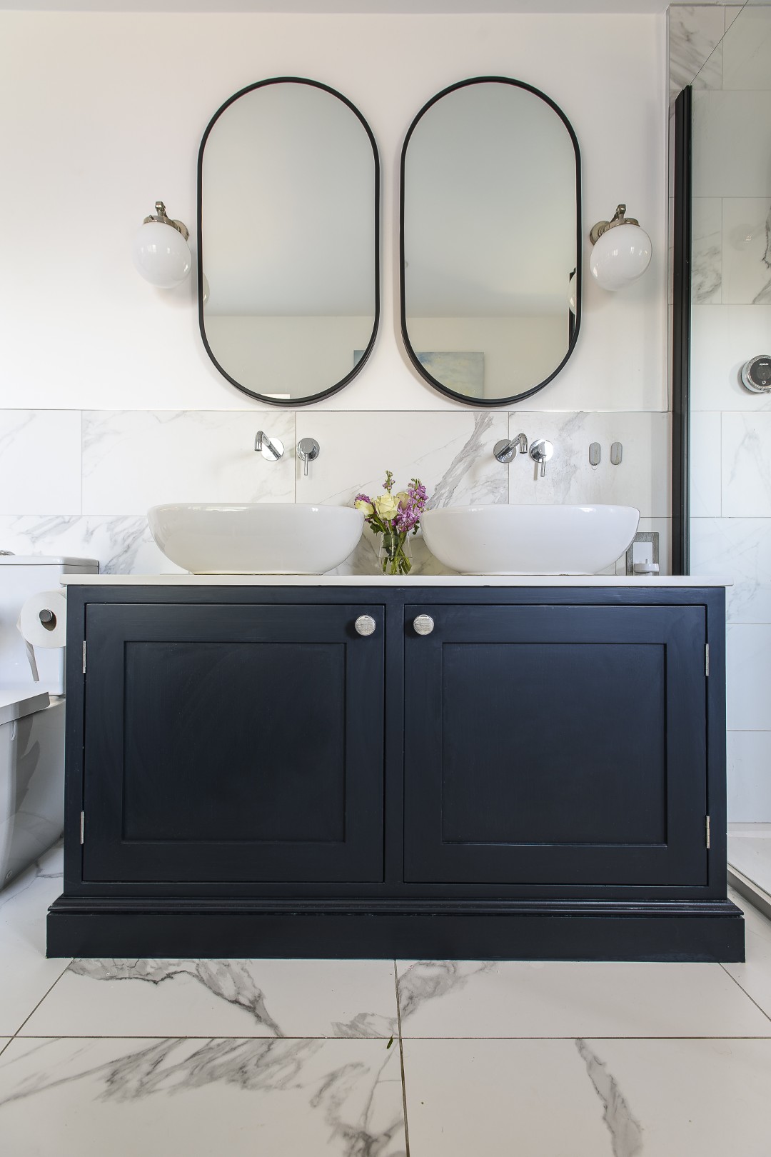 The pale and navy theme continues upstairs in the family bathroom, where marble tiles contrast with the deep blue basin unit