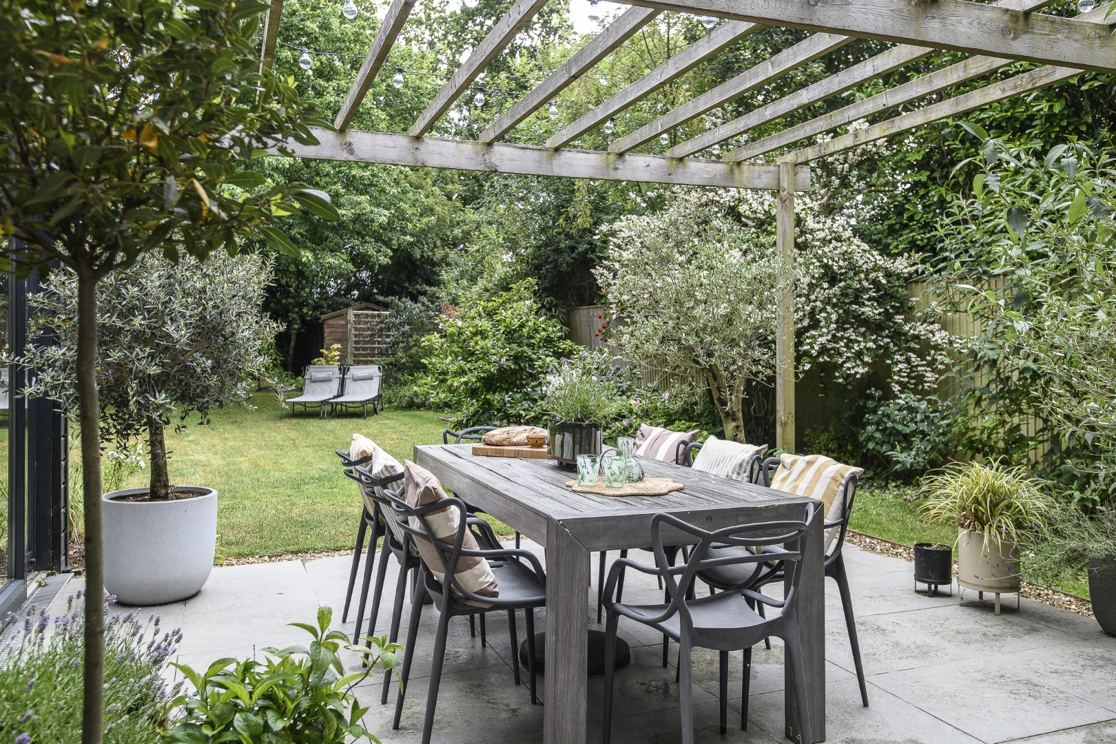 Large glass doors from the sitting room, and another set in the dining room, lead onto the patio and the garden beyond. Chairs by Kartell surround the dining table, padded with cushions from The Hus Edit.